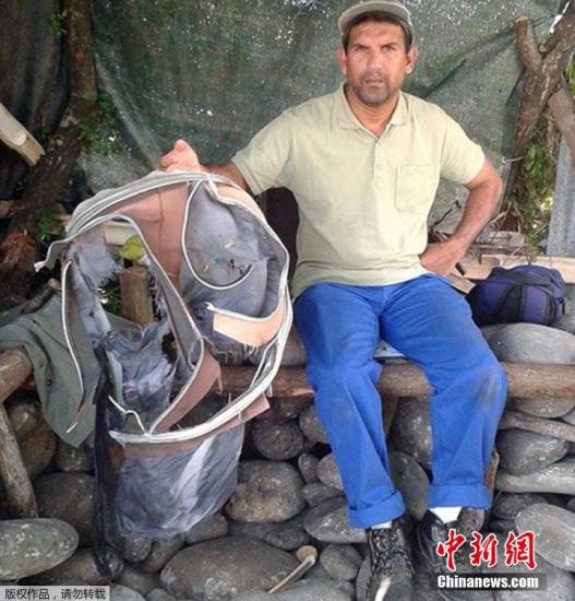 圖為當地時間7月30日，留尼旺島上的一名海岸清潔人員展示他找到的一個手提箱的殘骸。